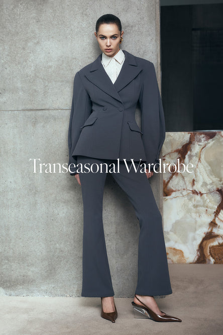 Woman in a gray suit standing against a textured wall.