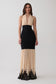 A woman modeling a sleeveless halter-neck maxi dress with a black fitted waist and skirt, and a sheer beige lower skirt with black lace trim at the hem, against a light gray studio background.