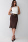 A woman modeling a dark brown knee-length pencil skirt with a scalloped lace hem and a matching dark brown belt with a gold buckle, paired with a white sleeveless top and dark brown heels.